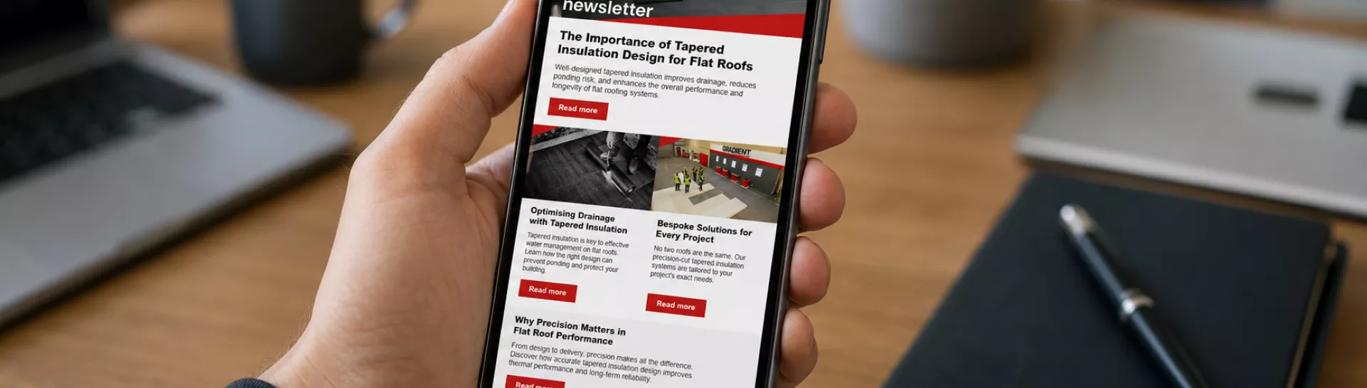 Person holding smartphone displaying a news app, desk items around.