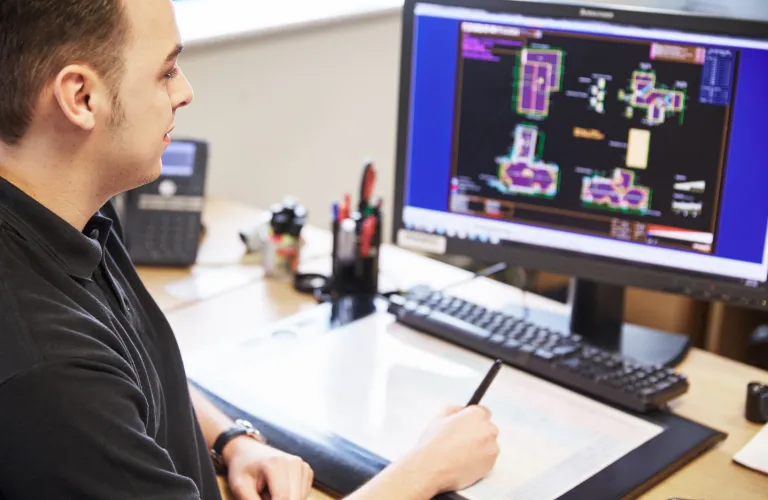 Man working on computer with technical drawings on screen.