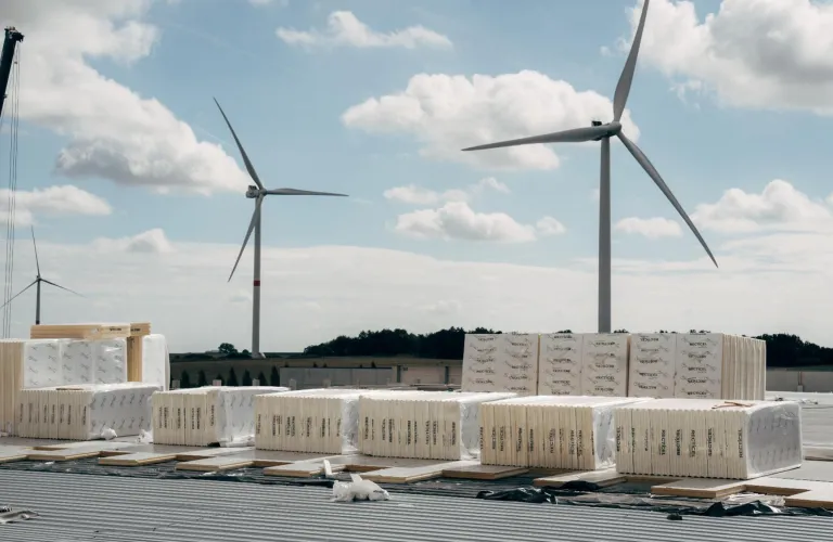 Wind turbines behind construction materials under blue skies.