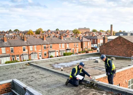 Workers inspecting a flat rooftop in a residential area.